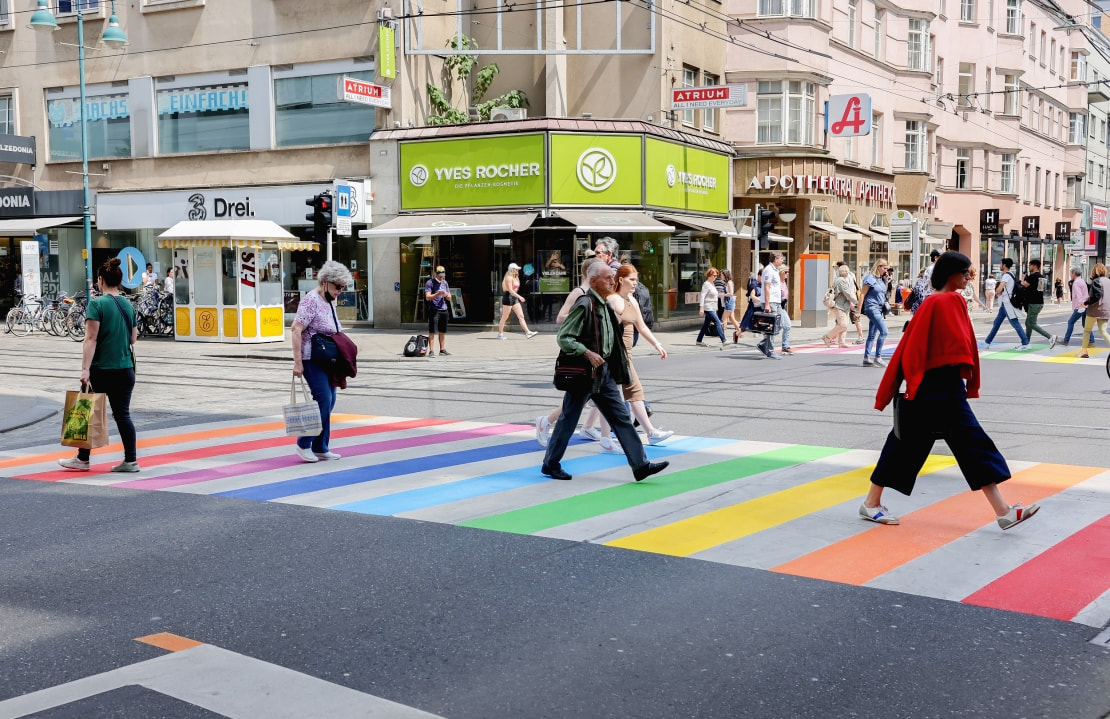 Mehrere Personen gehen über einen Zebrastreifen in der Linzer Innenstadt, der in den Regenbogenfarben als Zeichen für Toleranz leuchtet.